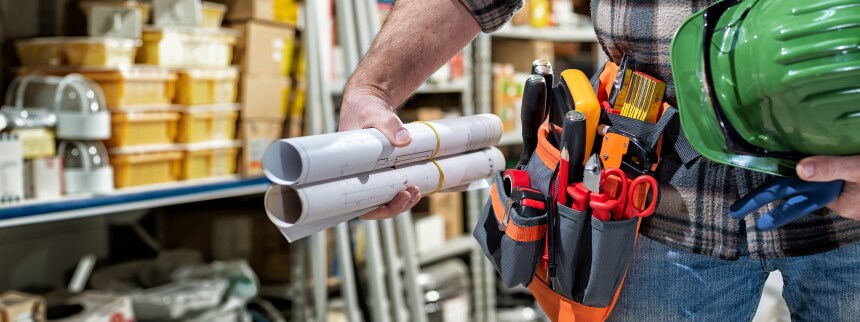 man holding tools, plans, and a hardhat